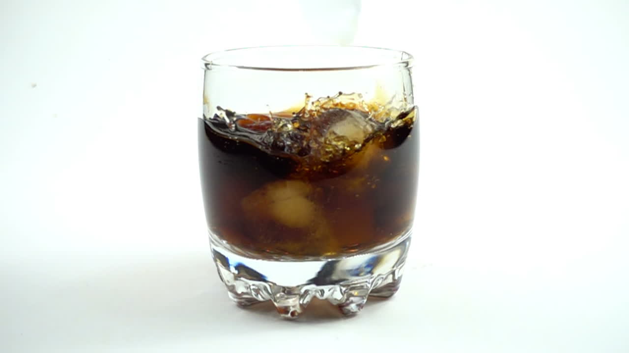Cubetti di ghiaccio cadono in un bicchiere con una Coca Cola. Rallentatore.