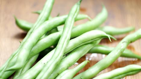 hand placing raw fresh uncooked string beans on wooden kitchen surface close up selective focus