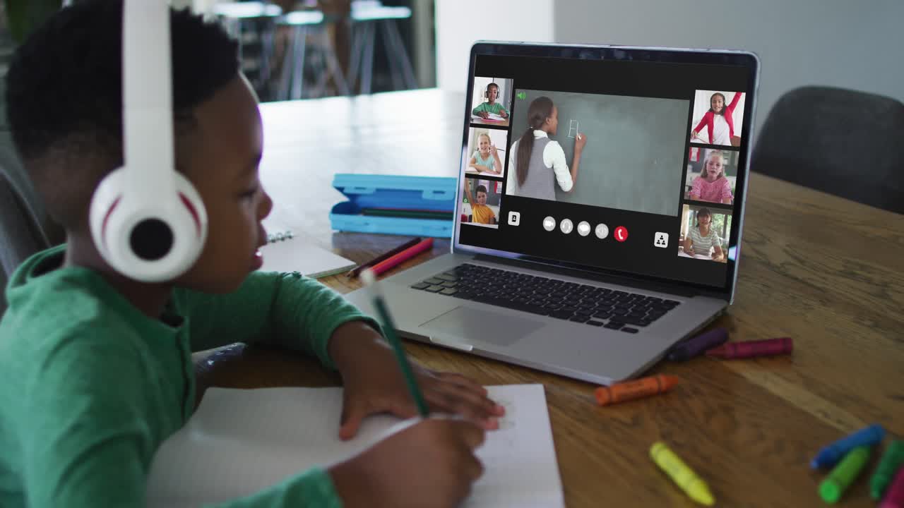 Schoolboy using laptop for online lesson at home, with diverse teacher and class on screen
