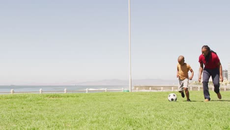 Video-Eines-Glücklichen-Afroamerikanischen-Vaters-Und-Sohnes,-Der-Draußen-Fußball-Spielt-Und-Spaß-Hat