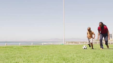 video of happy african american father and son playing soccer outdoors and having fun