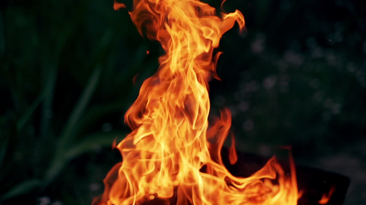 Orange tongues of flame with flying small sparks at night. Vivid flame of firewood burning on black background.