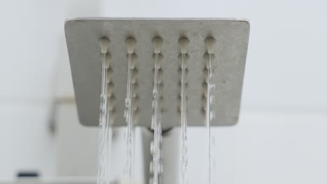 primer plano chorro de ducha con gotas de lluvia cayendo baño de baldosas blancas hasta cerrar se detiene disparo lento en el enfoque