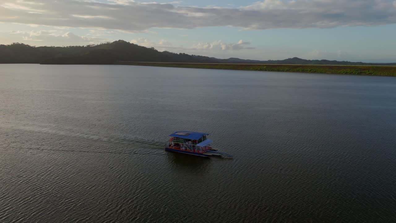 Ferry sailing on Hatillo Dam reservoir at sunset, Dominican Republic. Aerial drone orbiting, copy space