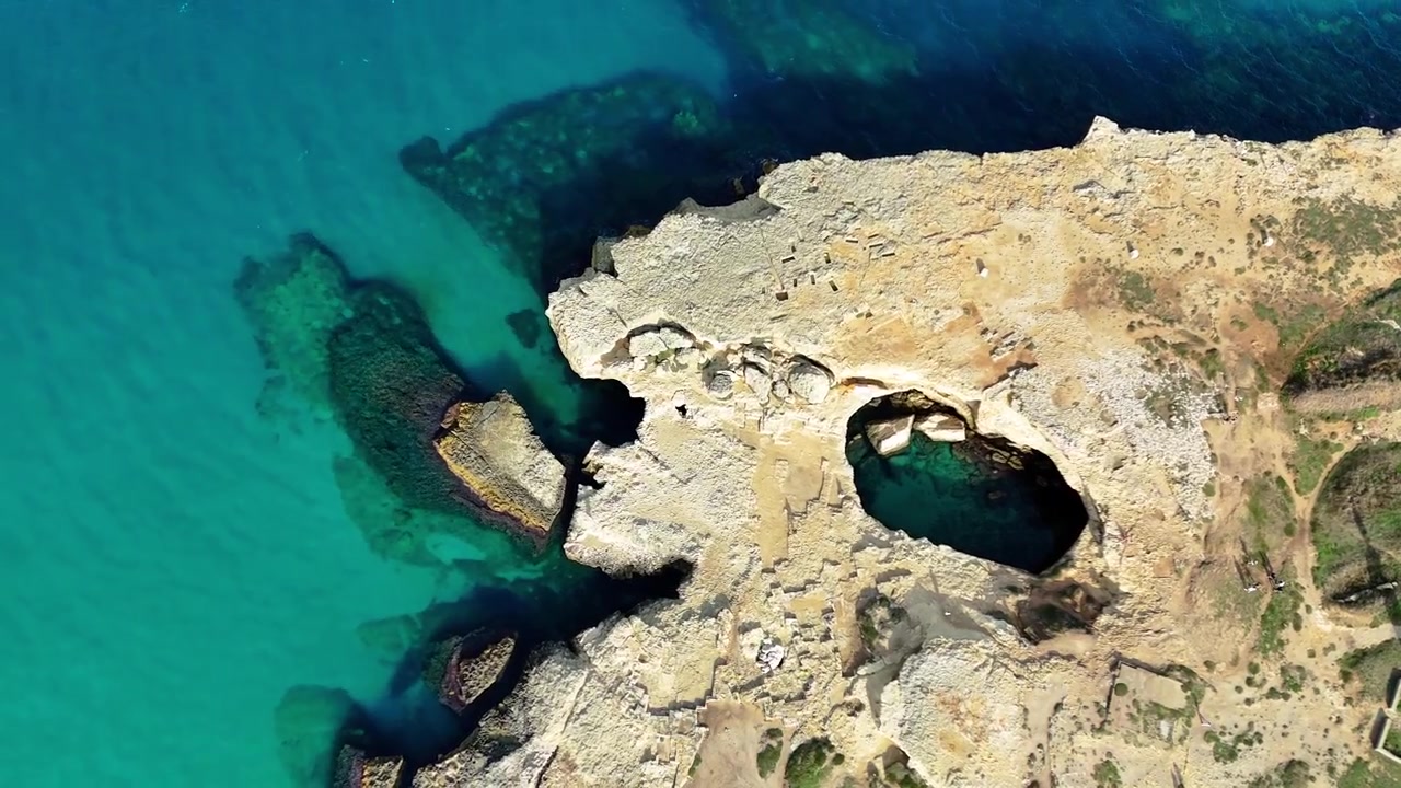 Ripresa zenitale con zoom out e semi-orbita del drone che rivela la Grotta della Poesia, una piscina naturale di calcare circondata da scogliere rocciose e dalle acque turchesi dell'Adriatico a Roca Vecchia, Puglia, Italia