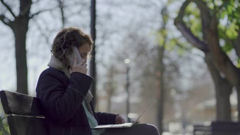 Cheerful-mature-woman-sitting-on-bench-and-talking-on-smartphone