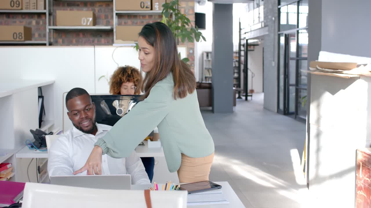 Felici colleghi diversi che usano il laptop e discutono di lavoro alla scrivania in ufficio, con spazio per il testo, al rallentatore.