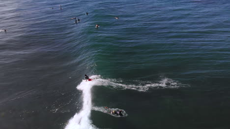 Surfer-riding-a-wave-while-it-is-crashing-in-the-blue-ocean-from-a-drone-during-a-clear-day-with-blue-sky