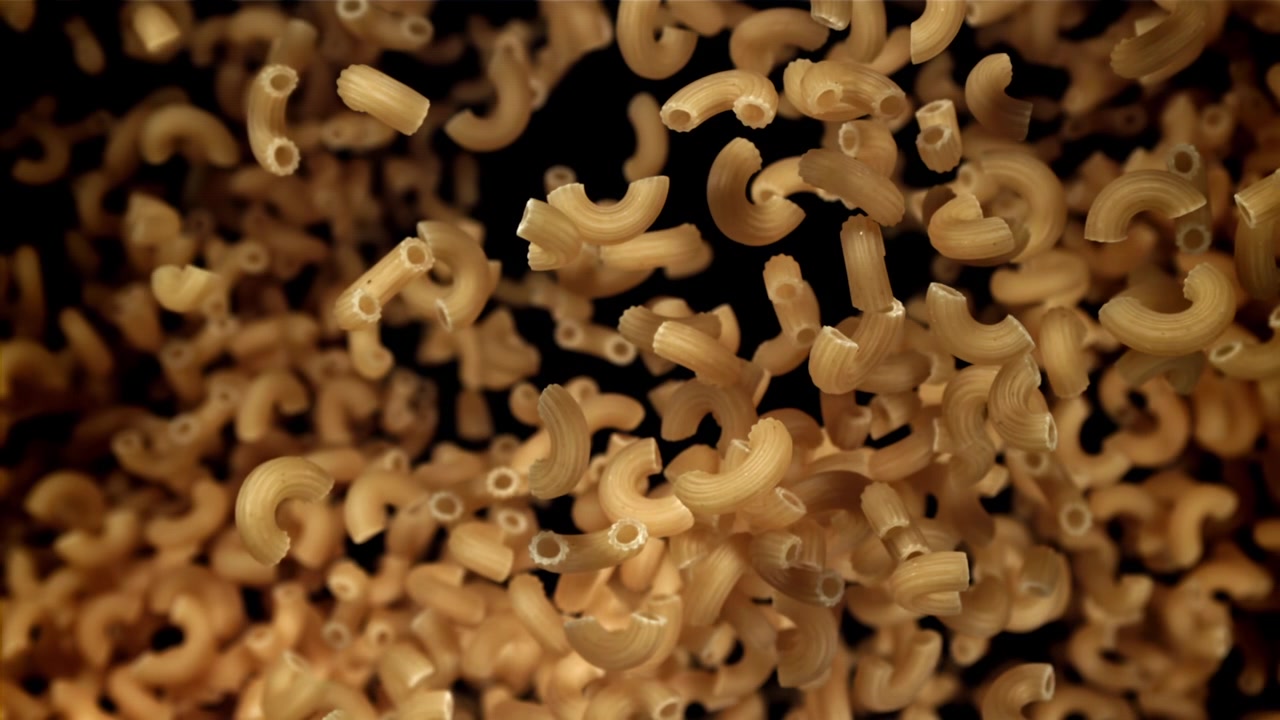 Pasta maccheroni secca che cade al rallentatore su sfondo nero.
