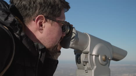 man looking through a telescope at a scenic viewpoint