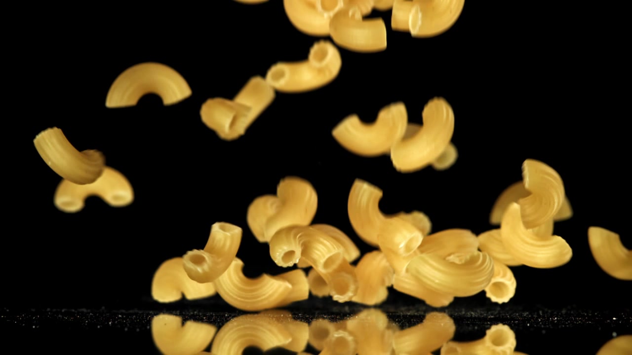 Maccheroni crudi che cadono al rallentatore su sfondo nero