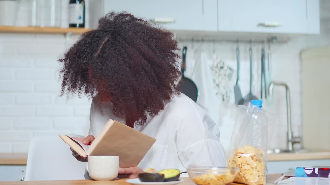 Young african american woman laughs reading book after breakfast