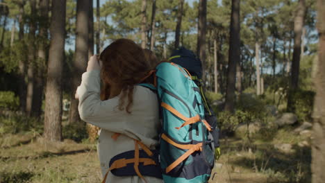 side view of two female friends with backpacks hiking together in the forest on a sunny day