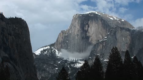 medium wide shot of yosemite's half dome hosting clouds and winter snow