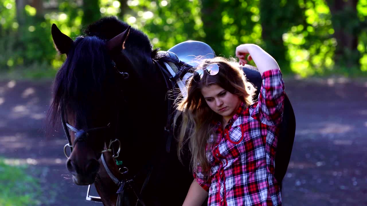 una joven rubia con una camisa a cuadros da un paseo con su caballo. una mujer que cuida de un caballo. noche soleada de verano.