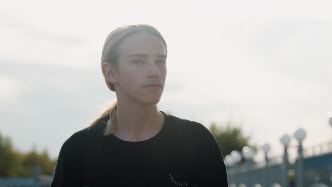 Thoughtful man observes sky. Caucasian individual deeply pondering under distant sky light. Man with dark shirt and ponytail reflecting emotionally amidst cinematic lighting conditions