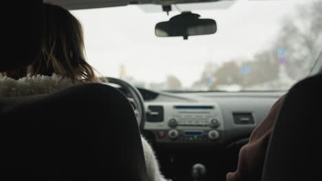 behind view of driver and passenger in moving car interacting and navigating city streets while holding steering wheel and blurred road signs, buildings, traffic lights visible through windshield