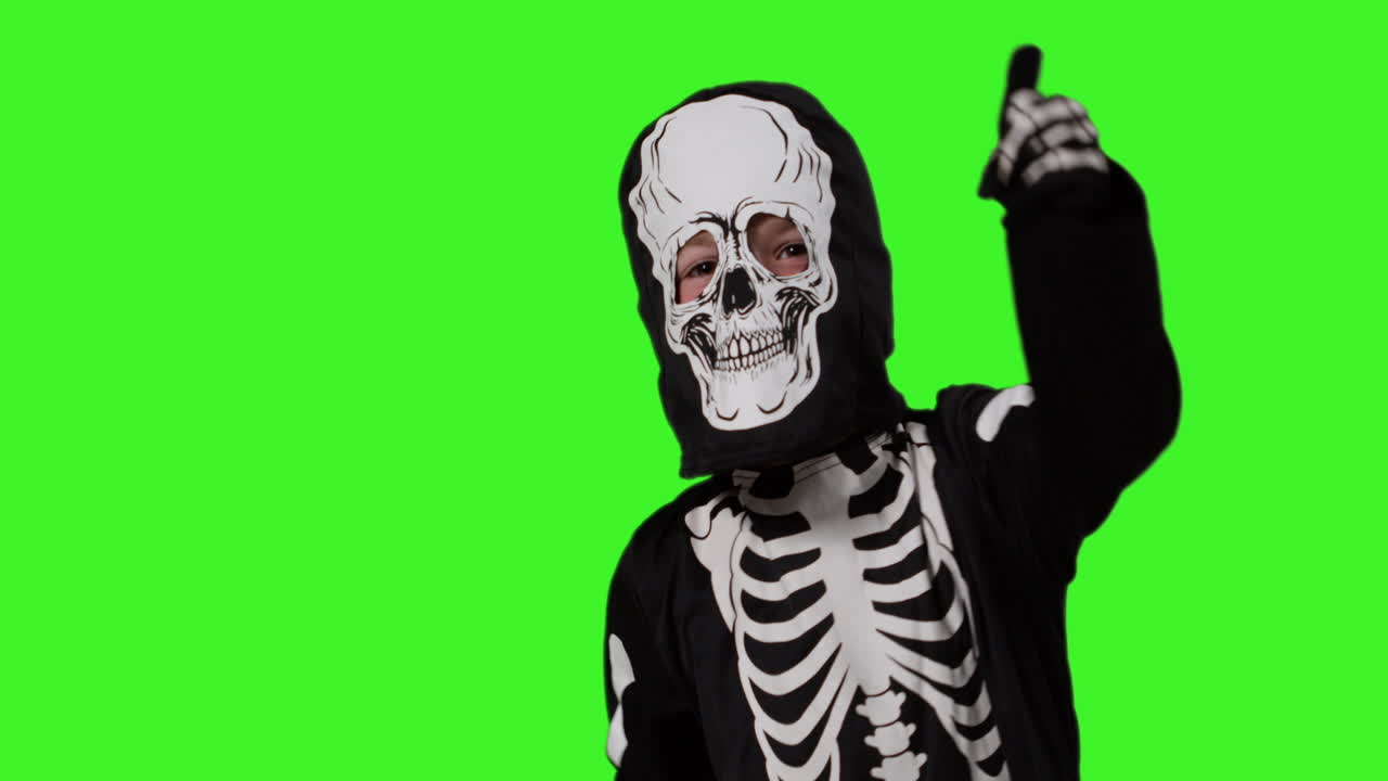 niño vestido con un disfraz de esqueleto teniendo un truco divertido o tratar en halloween bailando frente a la pantalla verde del estudio
