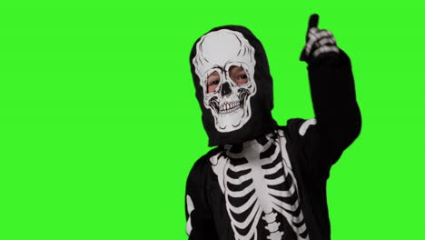 child dressed up in skeleton costume having fun trick or treating at halloween dancing in front of studio green screen