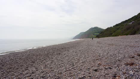 An-Einem-Diesigen-Tag-Schlendert-Ein-Entfernter-Wanderer-Am-Ruhigen-Kiesstrand-Von-Branscombe-In-Devon-Entlang