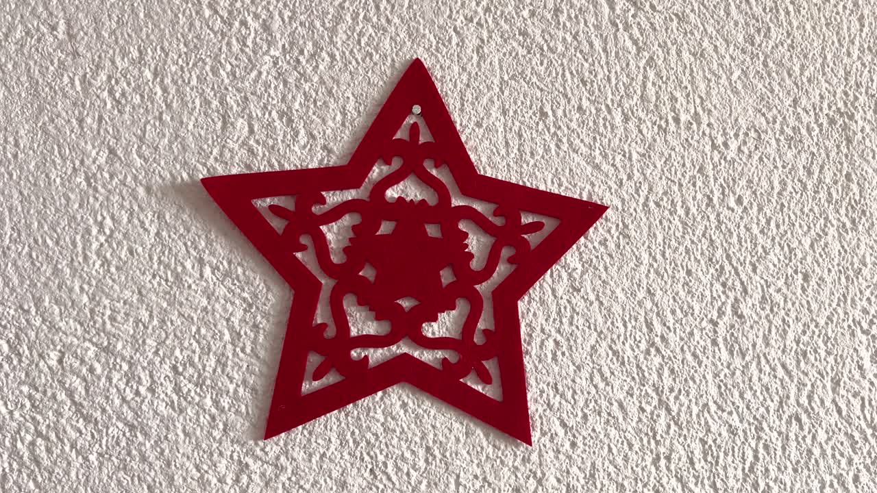 A red Christmas star made of felt hanging on a white wall. Red and white colors. Simplicity. Illustrative. Central composition