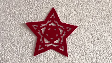 a red christmas star made of felt hanging on a white wall. red and white colors. simplicity. illustrative. central composition