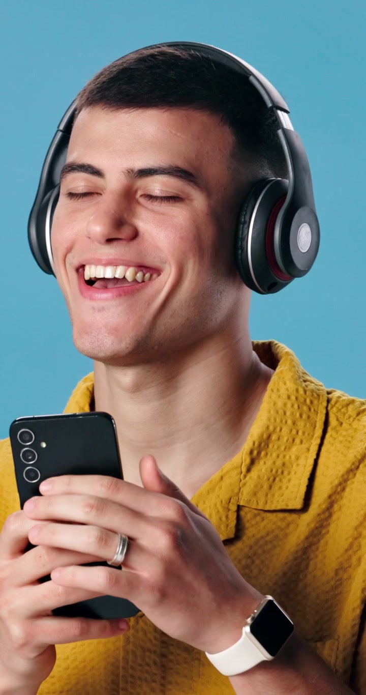 Giovane uomo con le cuffie che ride guardando lo smartphone