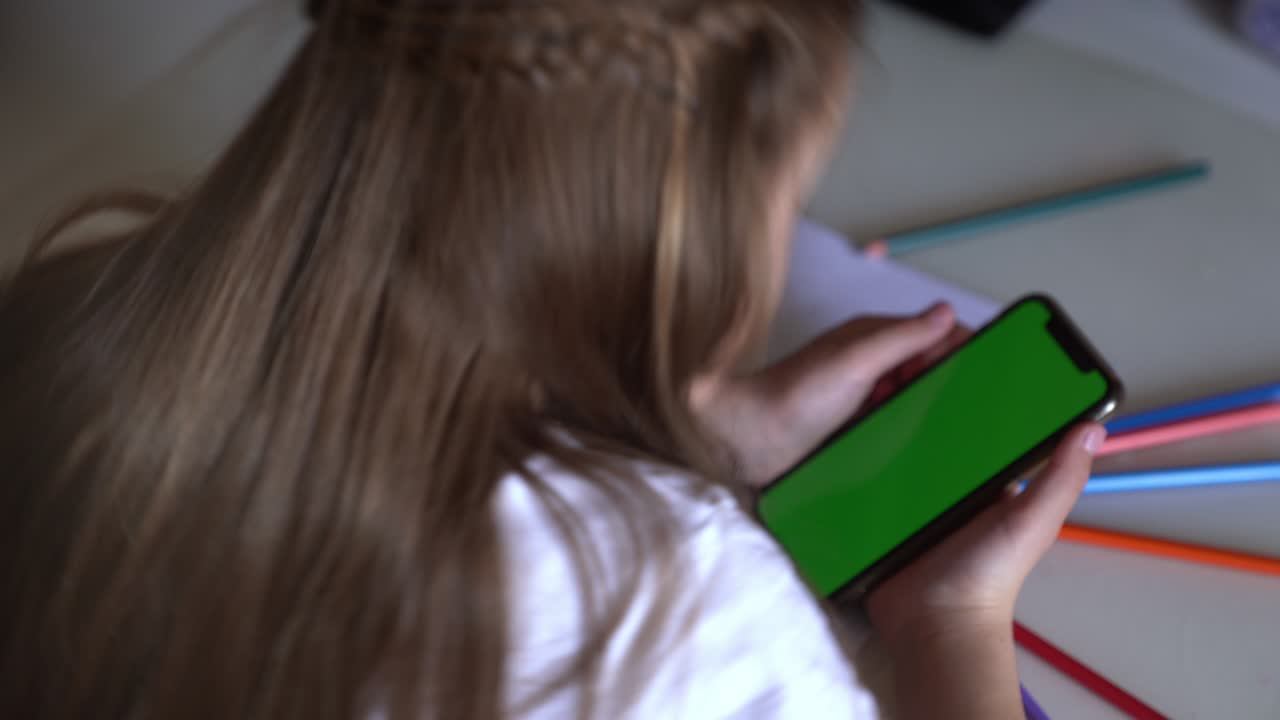 A little girl is sitting at a table with phone in hands, she looks at the Chroma