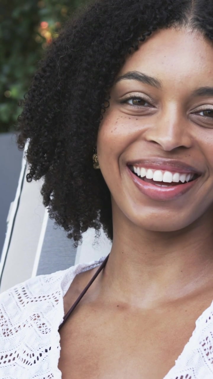 Mulher afro-americana sentada em cadeira listrada perto de arbustos, usando saída de praia de crochê com tachas douradas