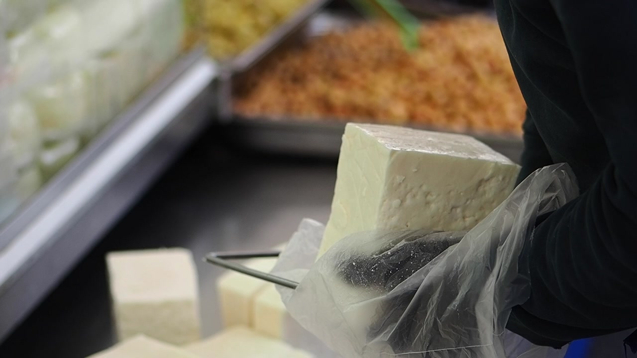 Person Cutting a Large Block of White Cheese with a Wire Cutter