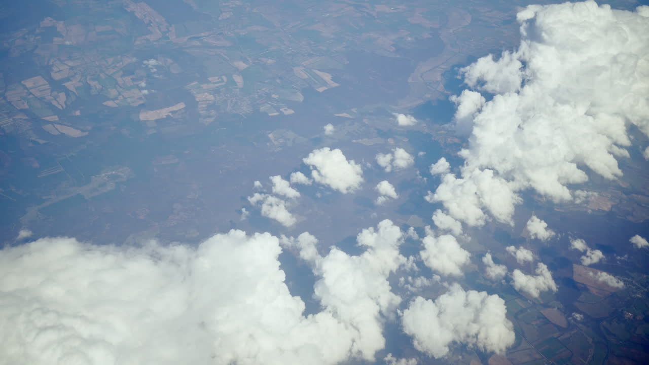 Aerial view of white, fluffy clouds above fields seen from an airplane window