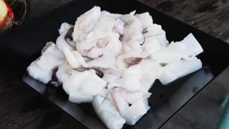 Fresh-raw-chopped-squid-on-plate-ready-for-cooking,-rotating-close-up