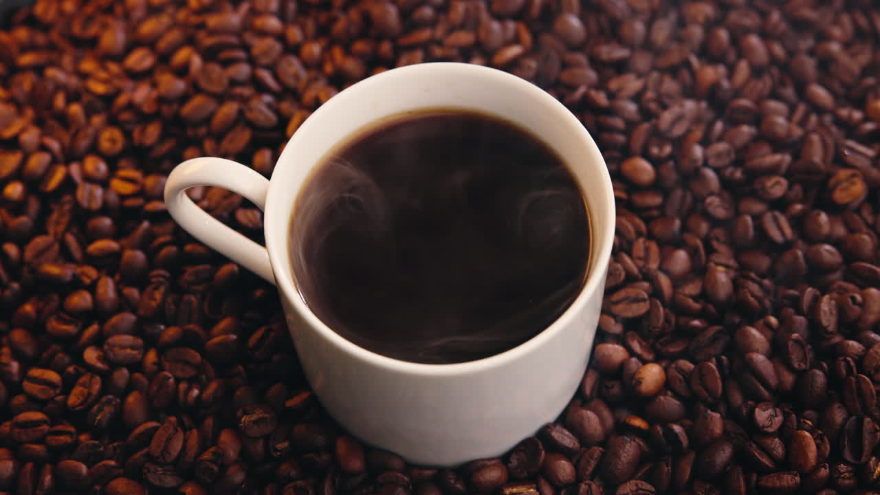 Café caliente humeante en taza blanca sobre granos de café tostados