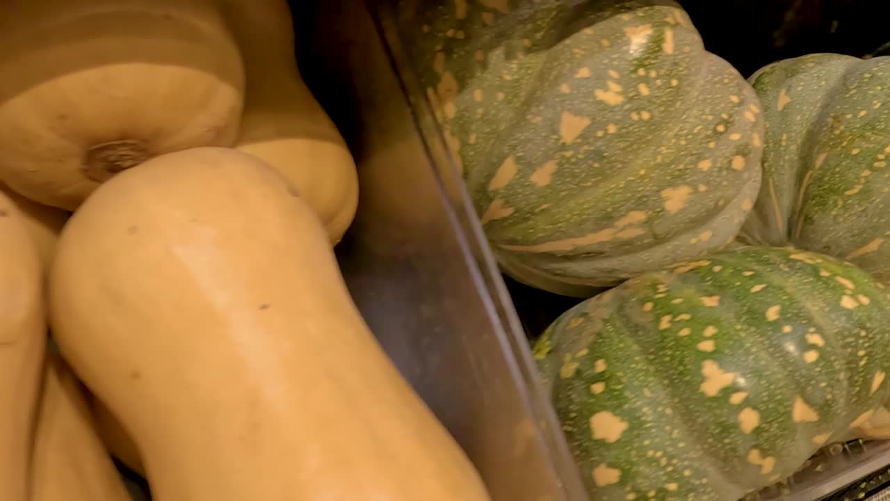 Une vue rapprochée détaillée de courges butternut fraîches et de potirons verts dans un étalage de supermarché.