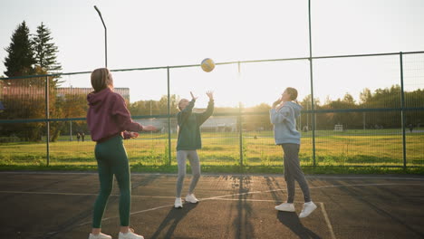 jugadores de voleibol principiantes practicando en una sesión al aire libre en una cancha con un campo de fútbol en el fondo, la luz del sol cálida proyectando largas sombras, mientras un jugador se prepara para golpear la pelota