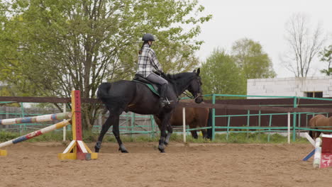 young female jockey riding black horse outside