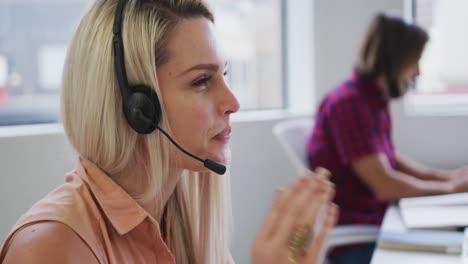 Caucasian-business-people-wearing-headphones-talking-to-customers-in-modern-office