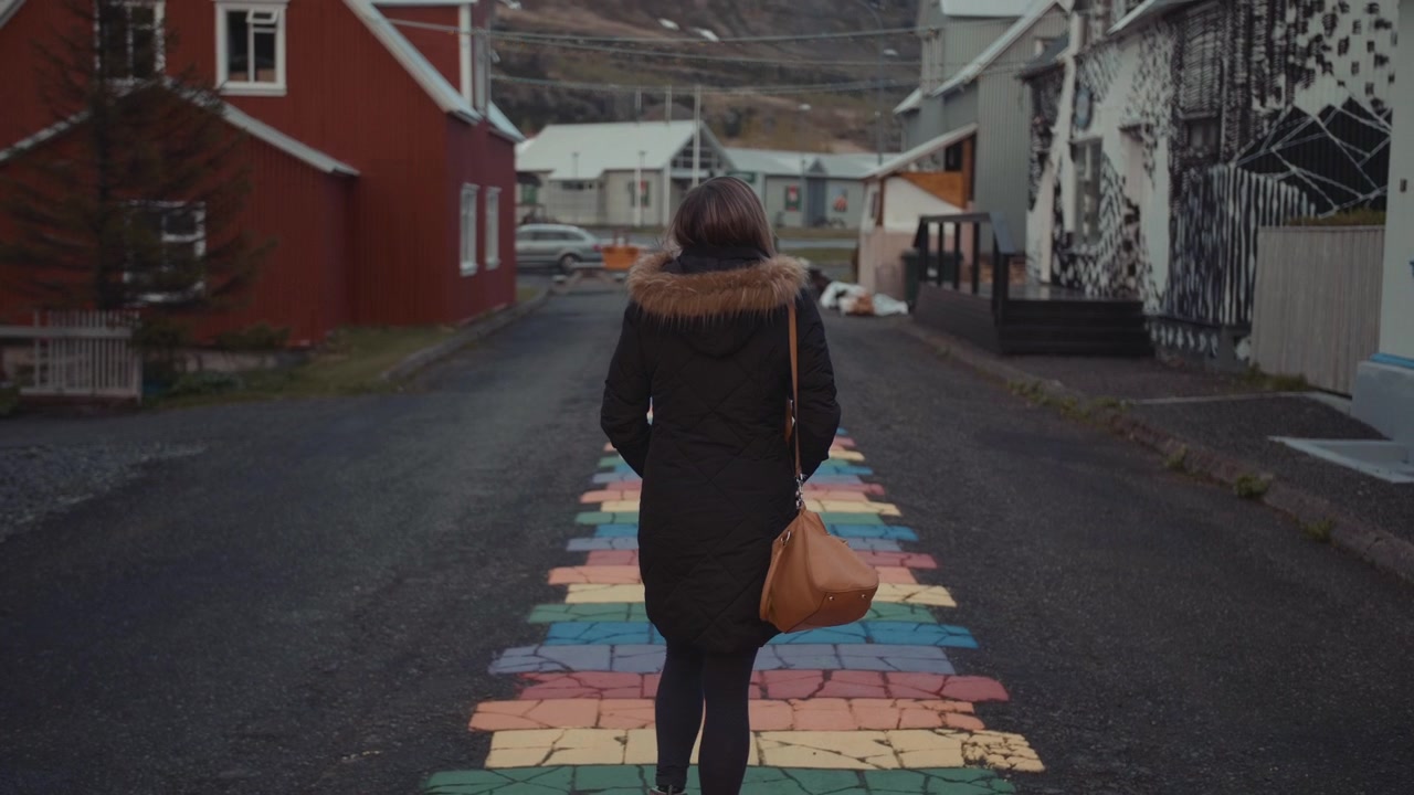 Vrouw loopt op een regenboogkleurige straat in een klein stadje