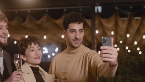 portrait of group of four happy multiethnic friends taking a selfie video and toasting with champagne glasses at new year's eve party 3