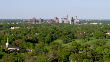 camera descends over a neighborhood and trees with a city skyline on the horizon