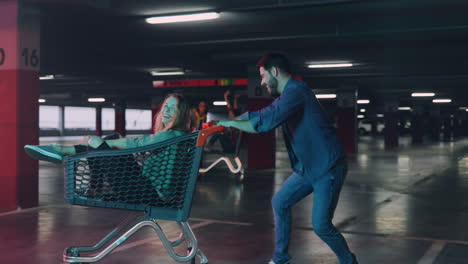 caucasian young couple having fun with a trolley in a parking and another couple coming up carrying a trolley