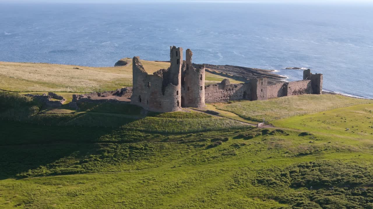 Aerial footage of Dunstanburugh castle ruins on a summer morning with no people