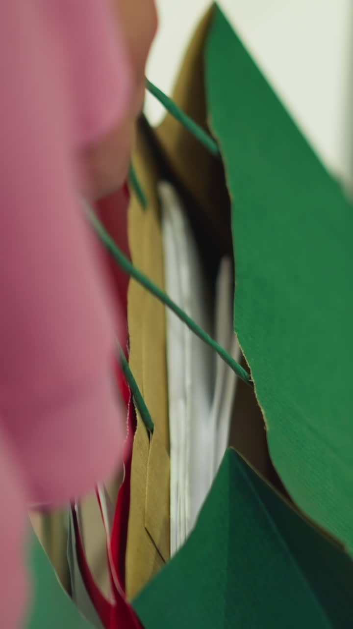 분홍색 드레스를 입고 다채로운 쇼핑 가방을 들고 있는 여성이 건물을 나가기 위해 문을 열고, 색 바지를 입은 사람이 뒤에서 부분적으로 보이고, 배경은 흐릿합니다.