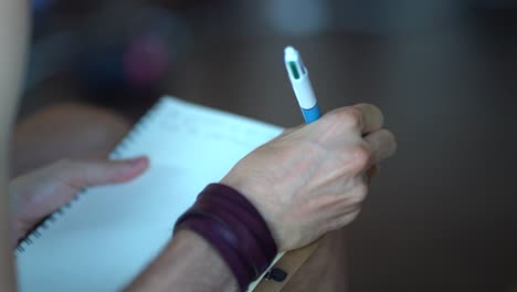 caucasian male writing with right hand on a white note book with multi color pen