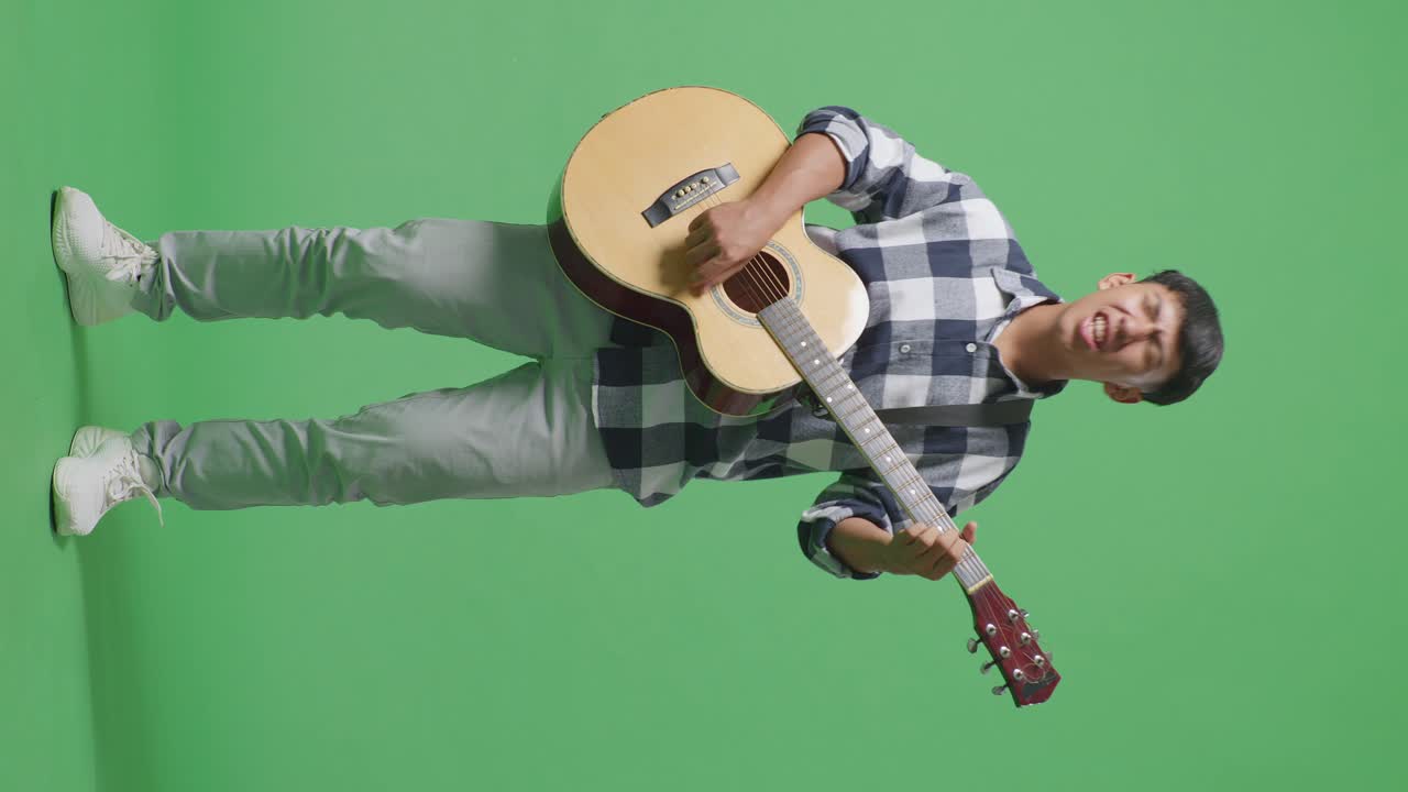 Figura intera di un giovane ragazzo asiatico adolescente che suona la chitarra con musica rock su sfondo green screen.