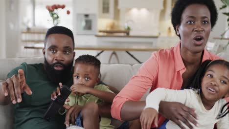 excited african american parents with son and daughter watching sport on tv at home, slow motion