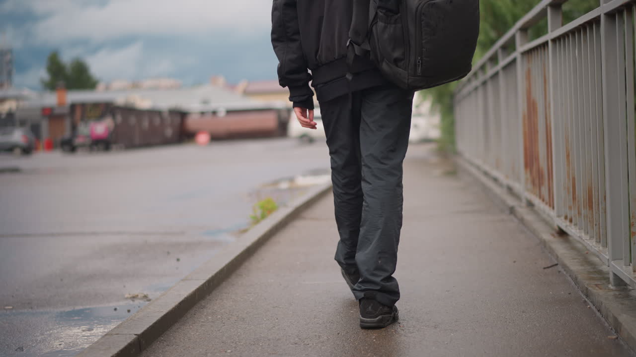 Primo piano di piedi che camminano su un marciapiede bagnato, vista a livello del suolo di scarpe da ginnastica macchiate di pioggia e passo lento, asfalto riflettente e sfondo cittadino attenuato catturano il movimento determinato di un pendolare.