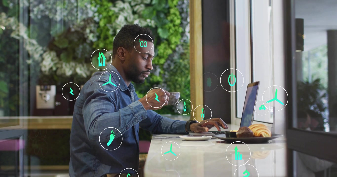 Man typing, sipping while green icons appearing lower left floating over laptop showing energy data