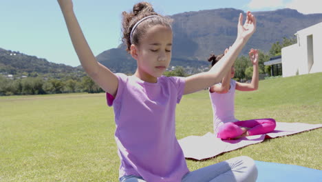 two biracial girls practice yoga outdoors, mountains in background