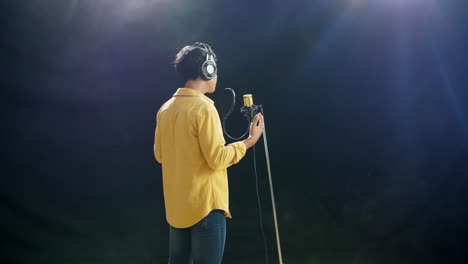 rücksicht auf einen jungen jungen mit kopfhörern, der in ein kondensatormikrofon auf dem weißen rauchschwarzen hintergrund singt